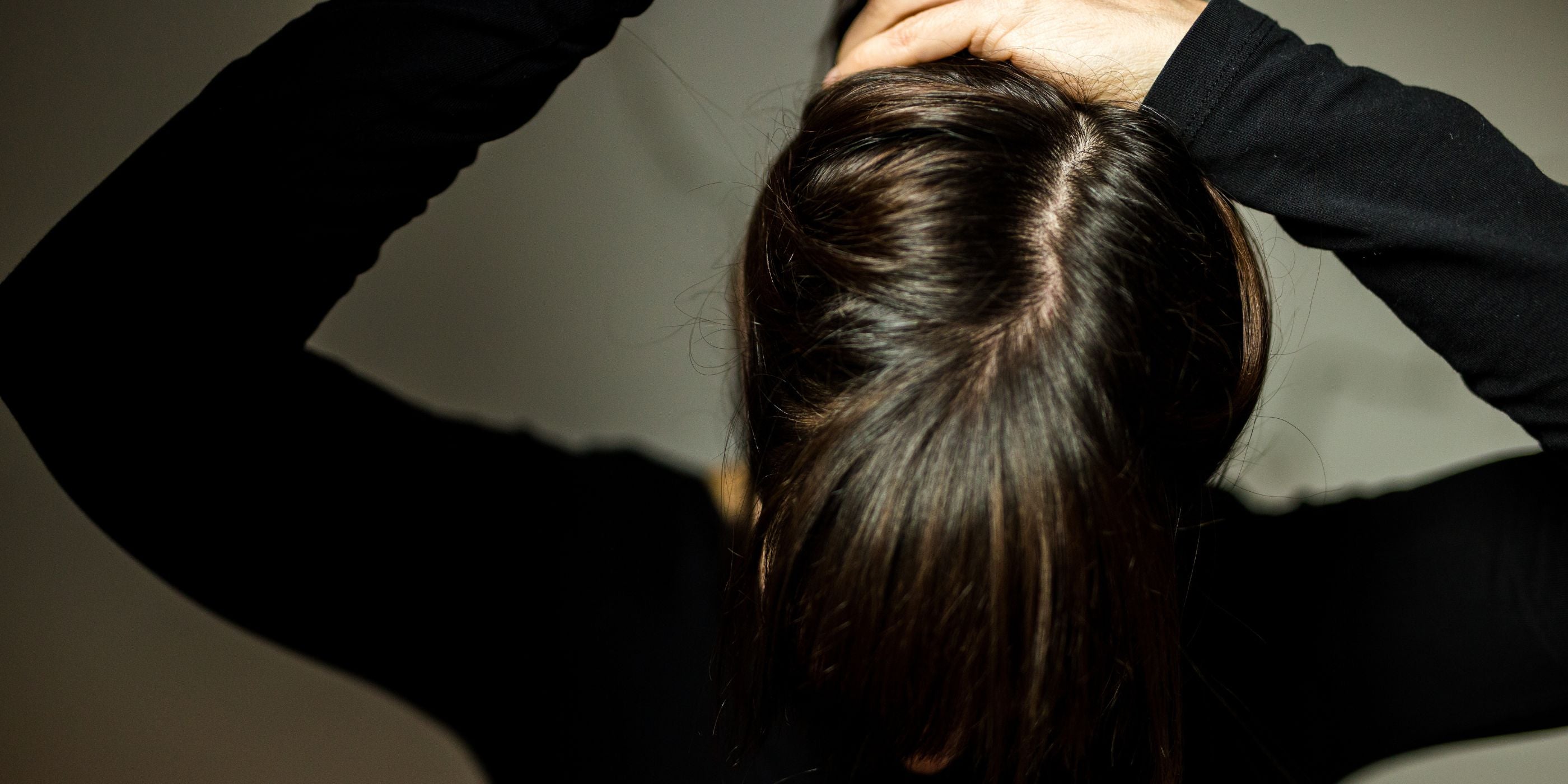weiblich gelesene Person von oben fotografiert hält ihre Haare zu einem Zopf zusammen